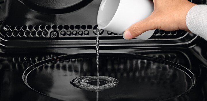 Un homme versant de l'eau dans le four vapeur multifonctions PlusSteam d'AEG